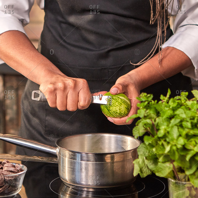 Professional confectioner cuts fresh lime peel into pan for cooking homemade dessert on a hob at the kitchen table. Step by step dessert making process.