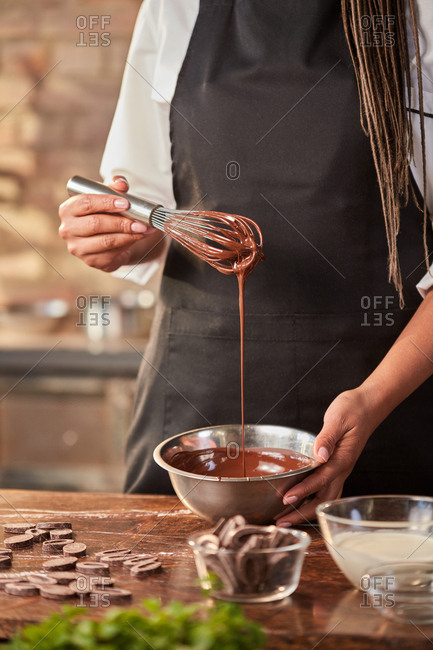 Female chef's hands in process of preparing desserts by whisk at the kitchen table against window. Concept of step by step process preparation of chocolate.