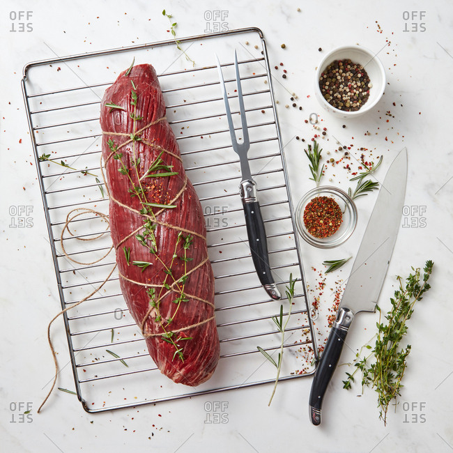 Fresh raw meat, whole piece of fillet with herbs and spices on a stone white background. Cooking ingredients for healthy organic meals. Top view.