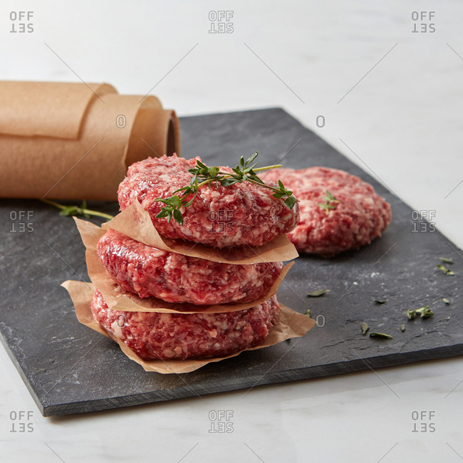 Cooking meat cutlets steaks for cooking homemade burgers with thyme, paprika, rosemary, olive oil on a  black slate plate on a white background.