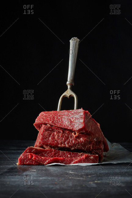 Freshly chopped natural raw veal fillet for roasting with meat fork on a shale board black background. Place for text.