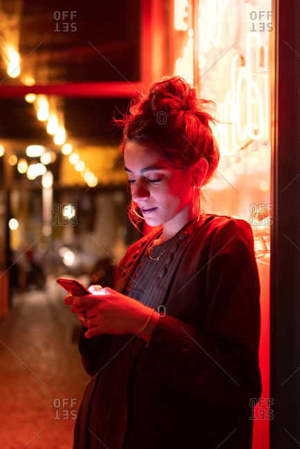 Attractive stylish lady using smartphone near neon lights
