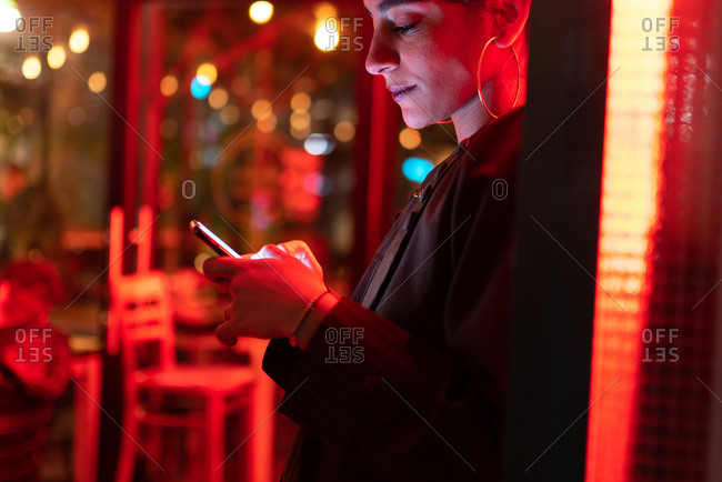 Attractive stylish lady using smartphone near neon lights