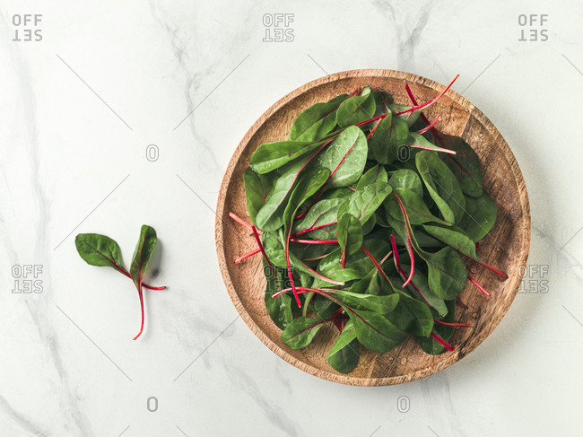 Fresh salad of green chard leaves or mangold on white marble background. Flat lay or top view fresh baby beet leaves on wooden plate. Copy space for text.