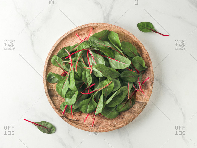 Fresh salad of green chard leaves or mangold on white marble background. Flat lay or top view fresh baby beet leaves on wooden plate. Copy space for text.