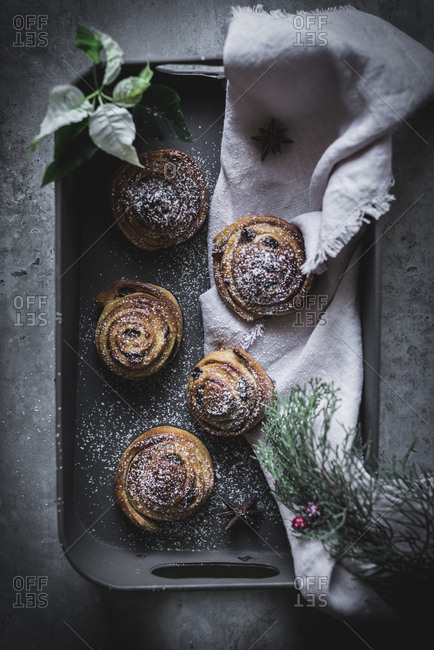 From above fresh herbs and piece of cloth lying on tray with yummy cinnamon rolls on gray surface