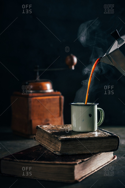 Poring hot coffee in an enamel cup with steam on dark mood