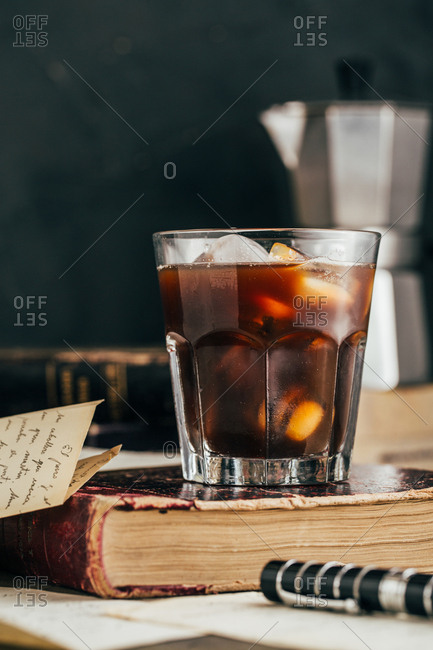 Cold espresso coffee glass in dark grunge mood with antique book
