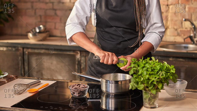 Professional confectioner cuts fresh lime peel into pan for cooking dessert on a hob at the kitchen table. Concept homemade sweets. Step by step dessert making process.