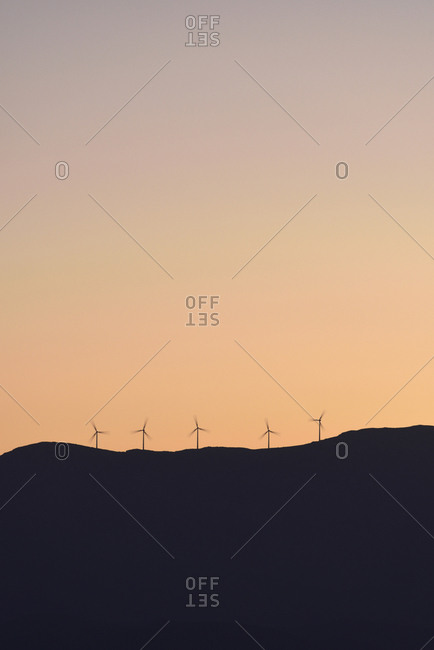 Silhouette of wind turbines on hill at sunset