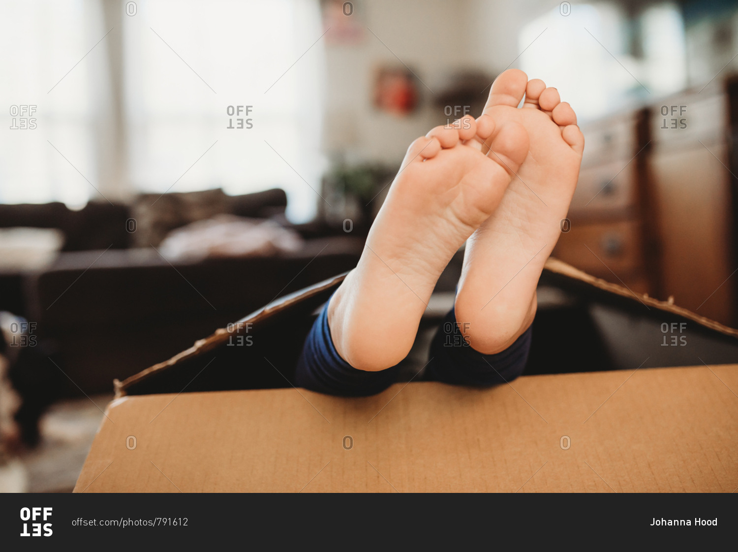 Bare feet of a little girl hiding in a box stock photo - OFFSET