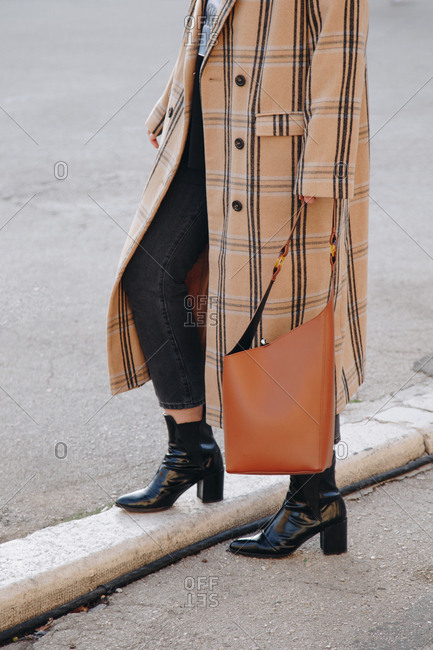 Fashion blogger outfit details. Portrait of young woman in the city, wearing an oversized plaid beige coat, dark jeans, black ankle shoes and a hobo bag.