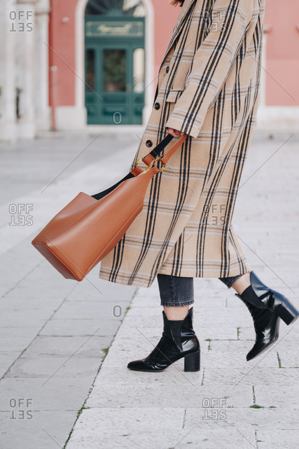 Fashion blogger outfit details. Portrait of young woman wearing oversized plaid beige coat, black ankle boots and hobo bag. Walking on the famous mediterranean square in the city of Split, Croatia.