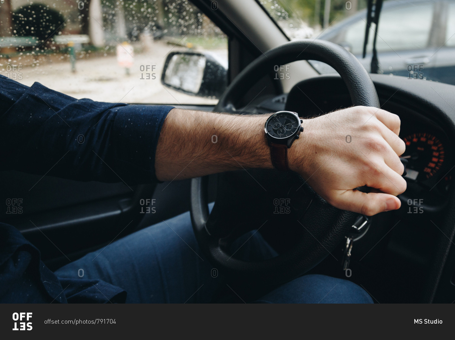 Man's hand holding the steering wheel of a car, wearing a modern wrist ...