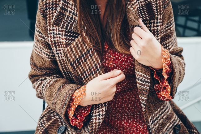 Fashionable young woman's hands straightening brown plaid coat that she's wearing over a red dot dress.