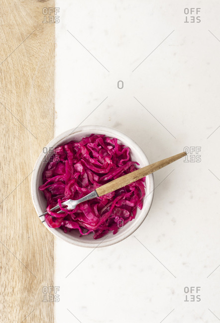 A bowl of sauerkraut with a fork on a marble and wooden board.