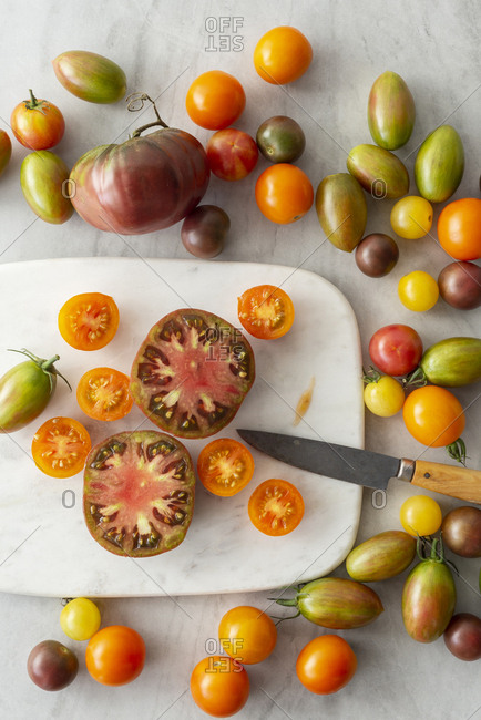 A range of tomato varieties, some cut open, on a marble cutting board with a knife.