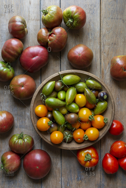 A variety of small and large garden-fresh tomatoes in a wooden bowl on a wooden table.