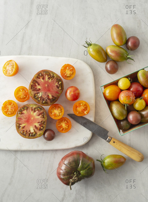A range of tomato varieties, some cut open, on a marble cutting board with a knife.