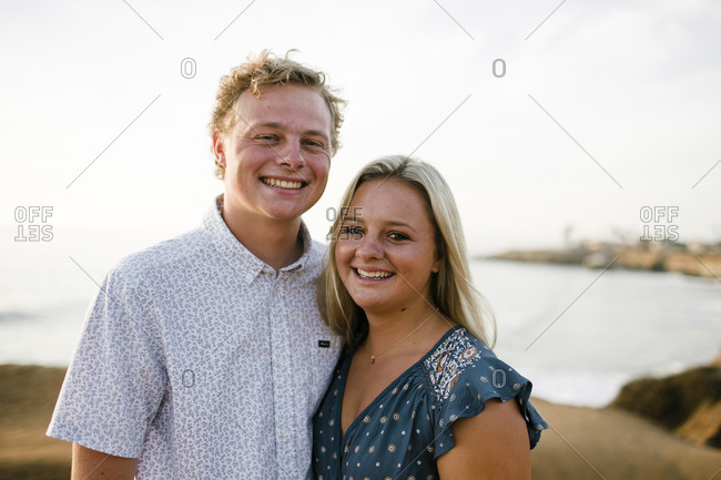 Portrait of happy siblings standing on cliff against sea during sunset