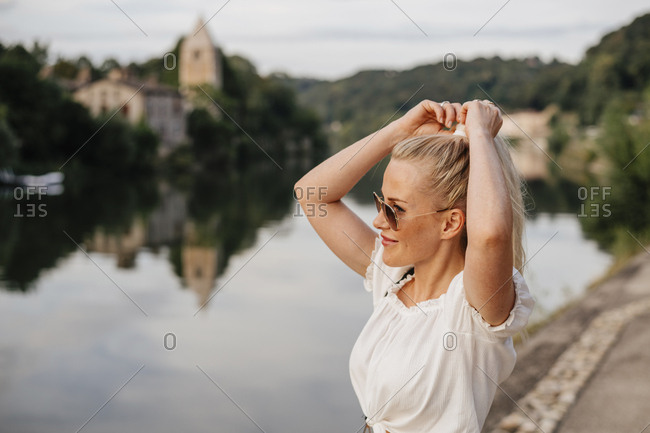 Smiling Woman Tying Hair While Standing By Saone River Against Sky