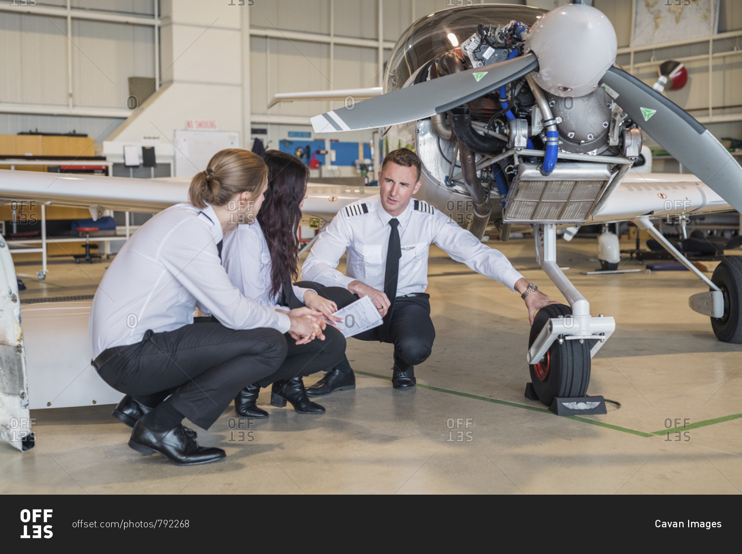 Male engineer showing airplane wheel to trainees while crouching on floor in hangar