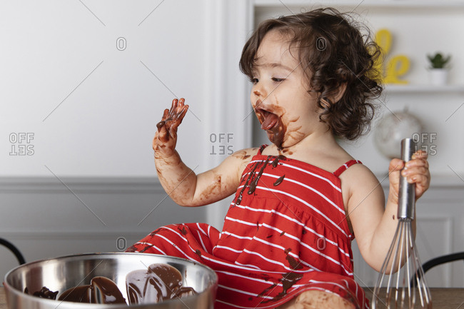 Messy baby girl with mouth open sitting on table against wall at home