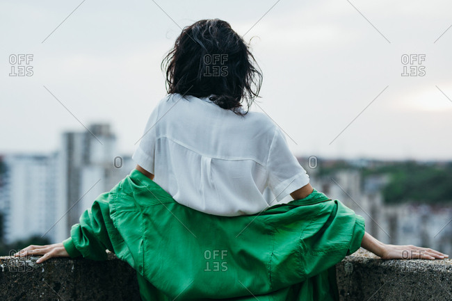 Back view of woman wearing green jacket standing on a rooftop.