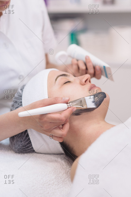 Cosmetician putting black face mask to the client