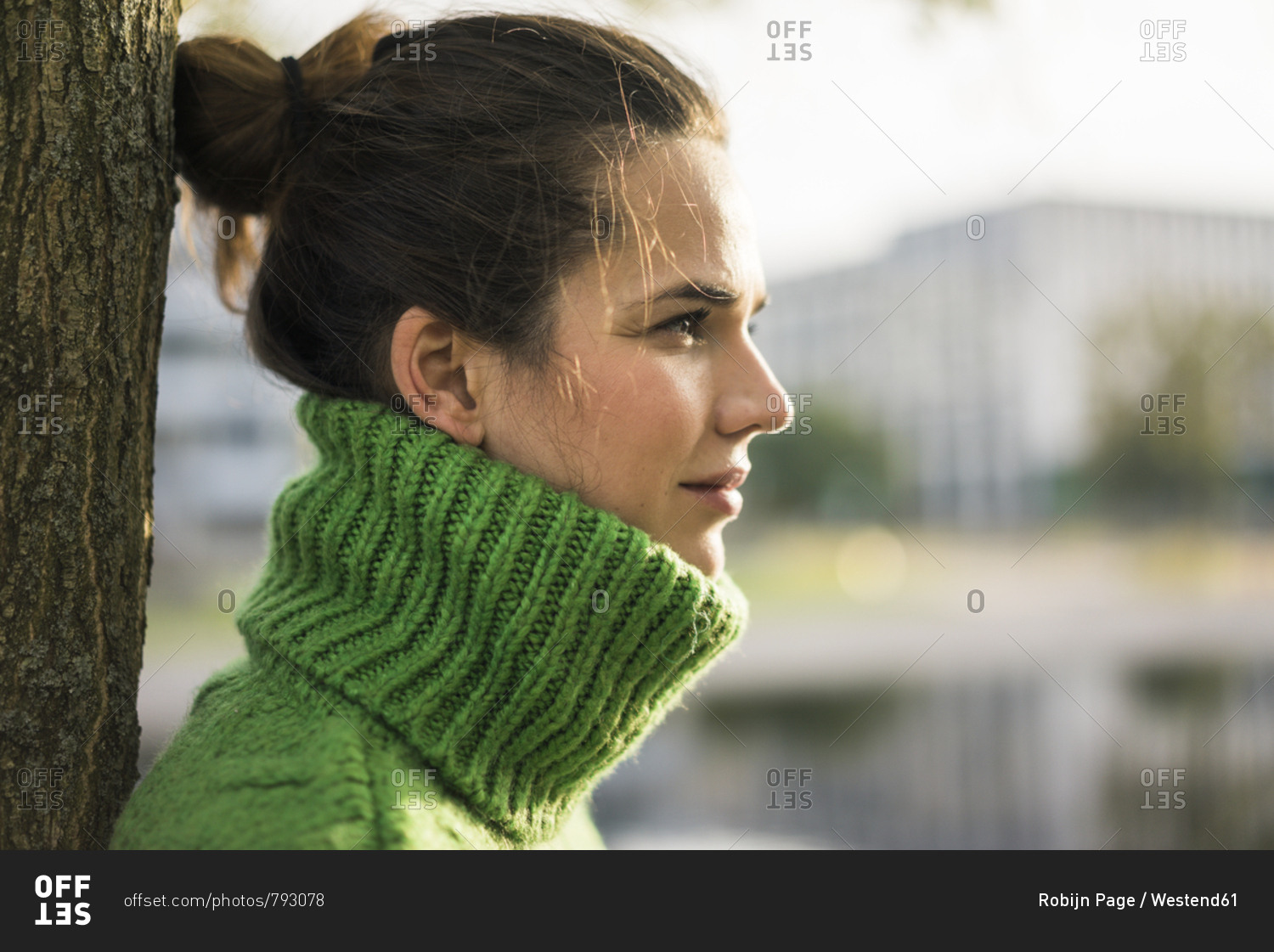 Profile of relaxed woman wearing green turtleneck pullover leaning against tree trunk