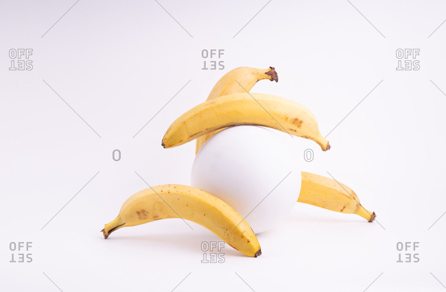 Composition with bananas and plaster sphere on white background