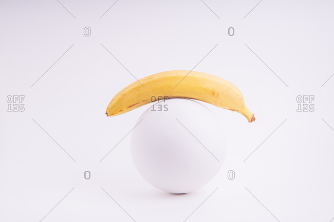 Composition with banana and plaster sphere on white background