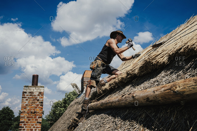 Man repairing thatch roof on sunny house
