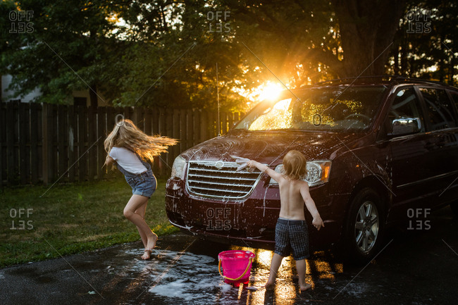 Two kids washing a minivan at sunset