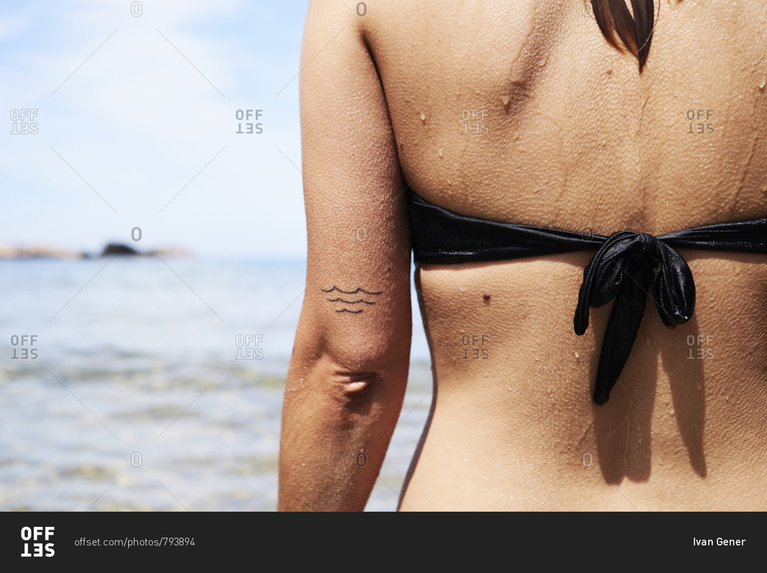 Back view of woman in black bikini top with goose bumps skin and wave tattoo