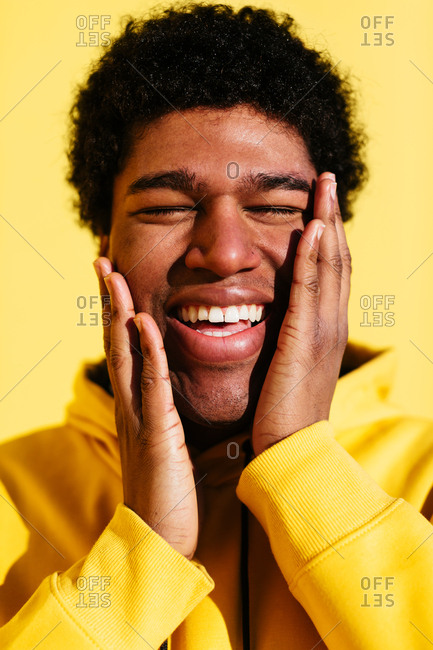 Smiling young african man wearing yellow hoodie on yellow wall.