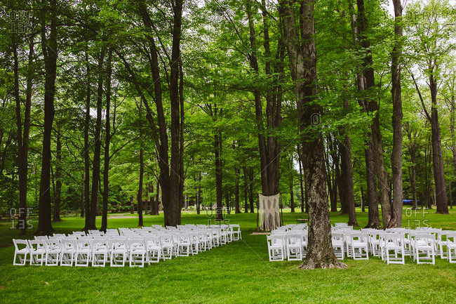 White chairs set up by trees in a rural wedding