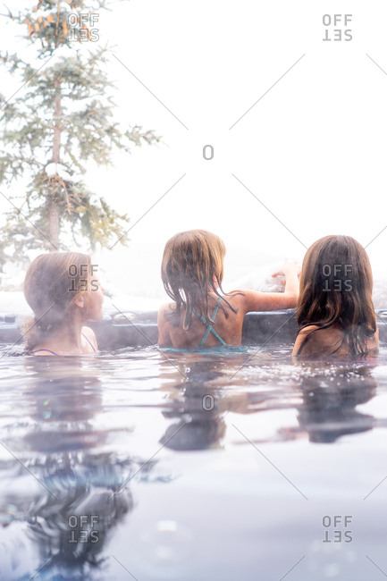 Rear view of three kids playing with snow in a hot tub outside during winter