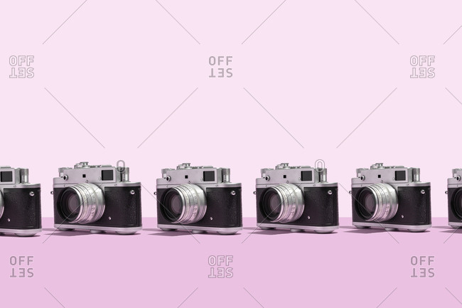Photo cameras organized in a row over pink background