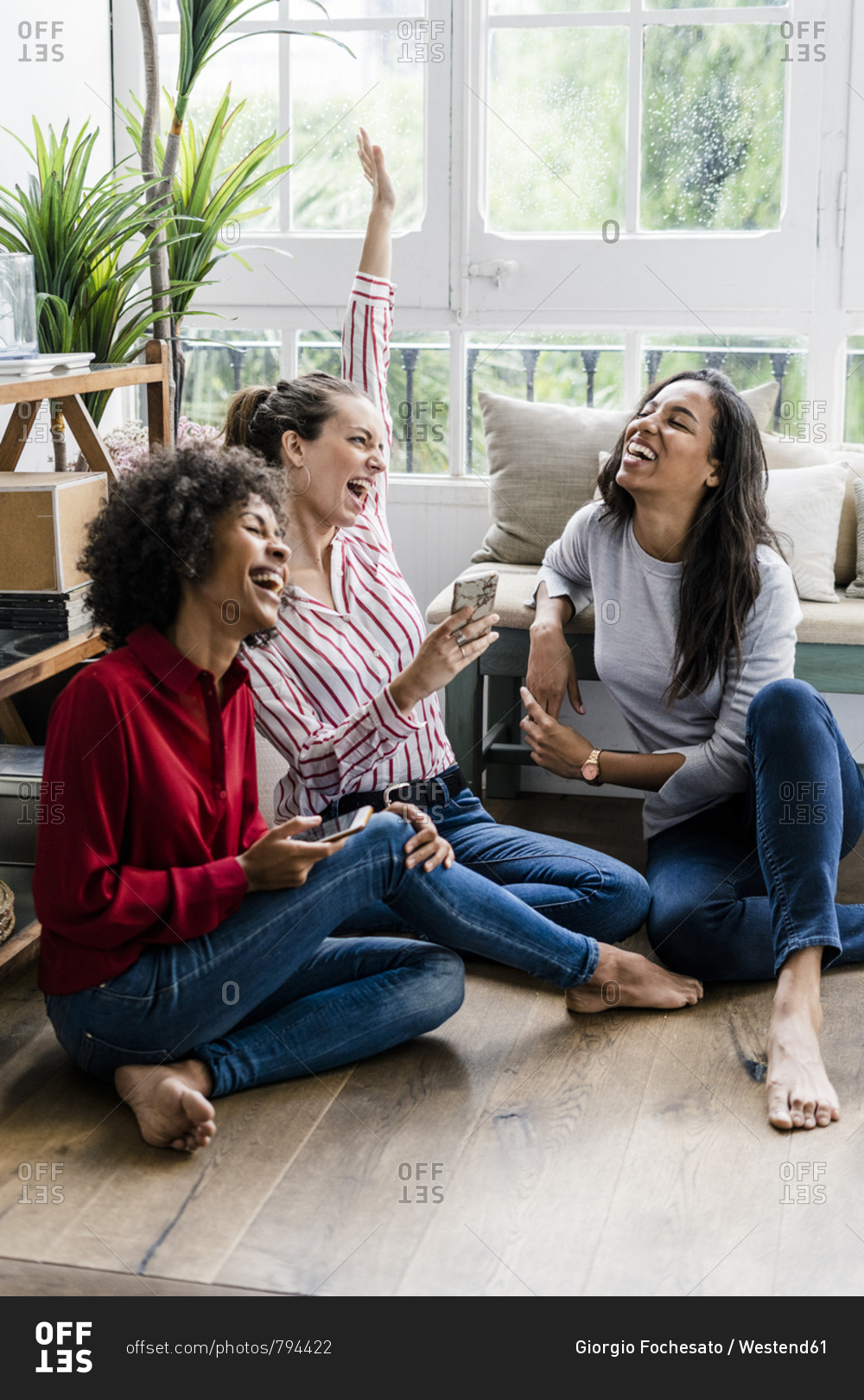 Three carefree women sitting on the floor at home with cell phones