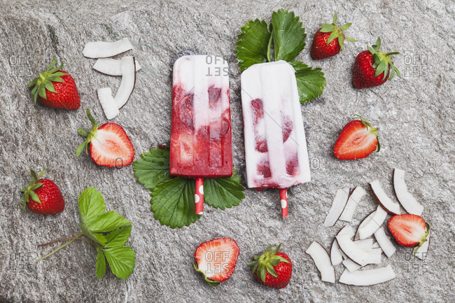 Homemade strawberry coconut ice lollies with fresh strawberries and coconut slices on granite