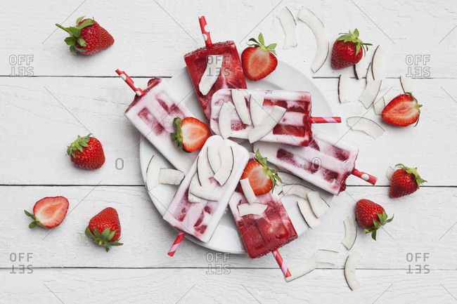 Homemade strawberry coconut ice lollies with fresh strawberries and coconut slices on plate