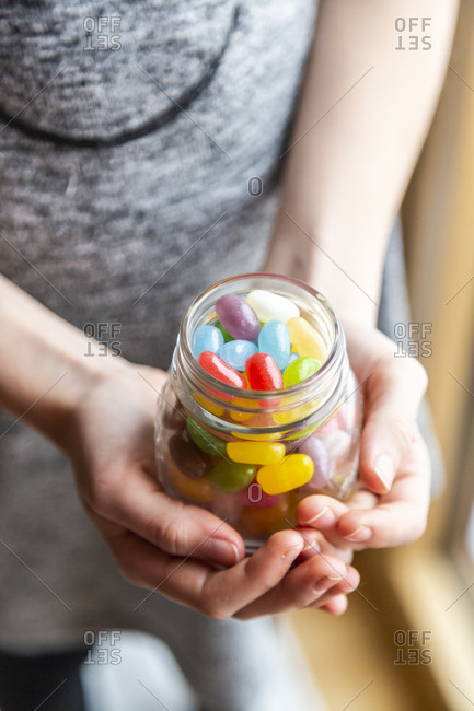 Glass of colourful sweet jellybeans on white wood- hands holding glass