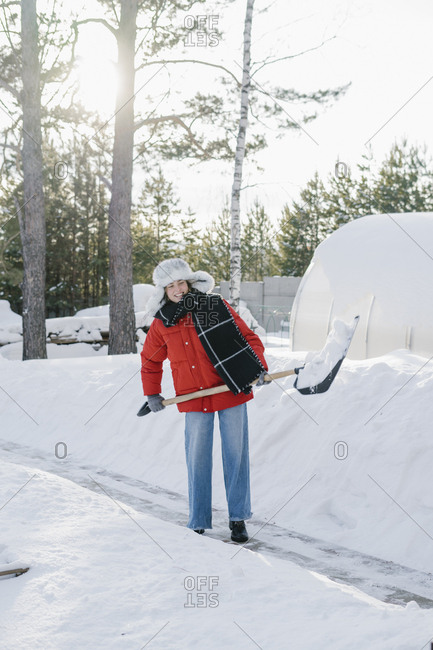 A woman in a fur hat shovels snow from a country house