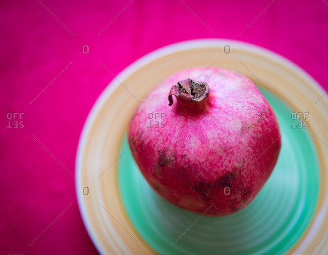 pomegranate in a dish set on a violet table.