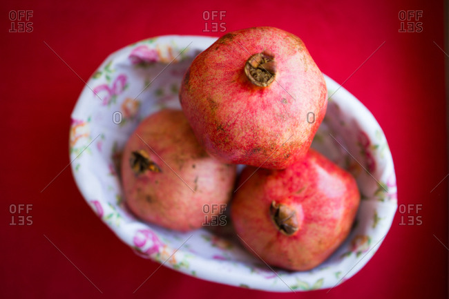 pomegranates in a floral dish set on a red table.