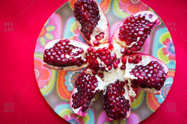 pomegranate split open on a floral dish set on a red table.