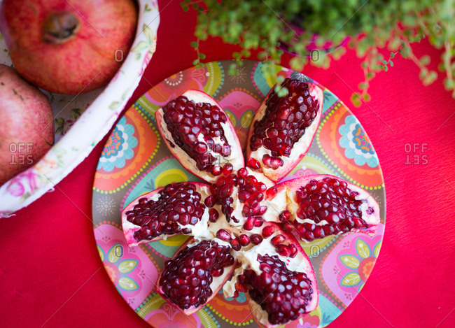 pomegranate split open set on a floral plate on a red table..