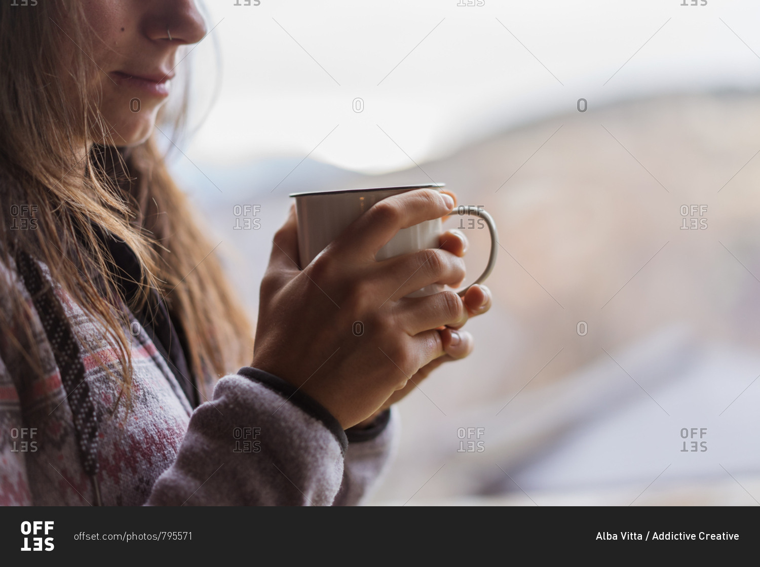 Side view of unrecognizable female in warm jumper smiling and enjoying hot beverage while standing near huge window at home