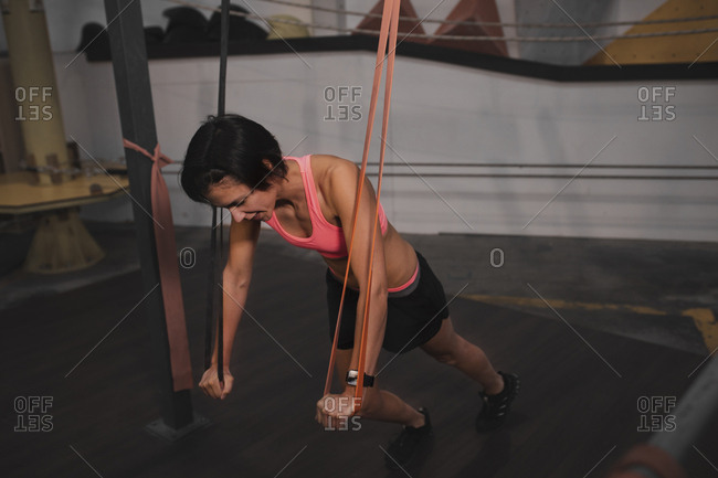 Young slim sportive lady in sportswear doing exercises with resistance band in gym